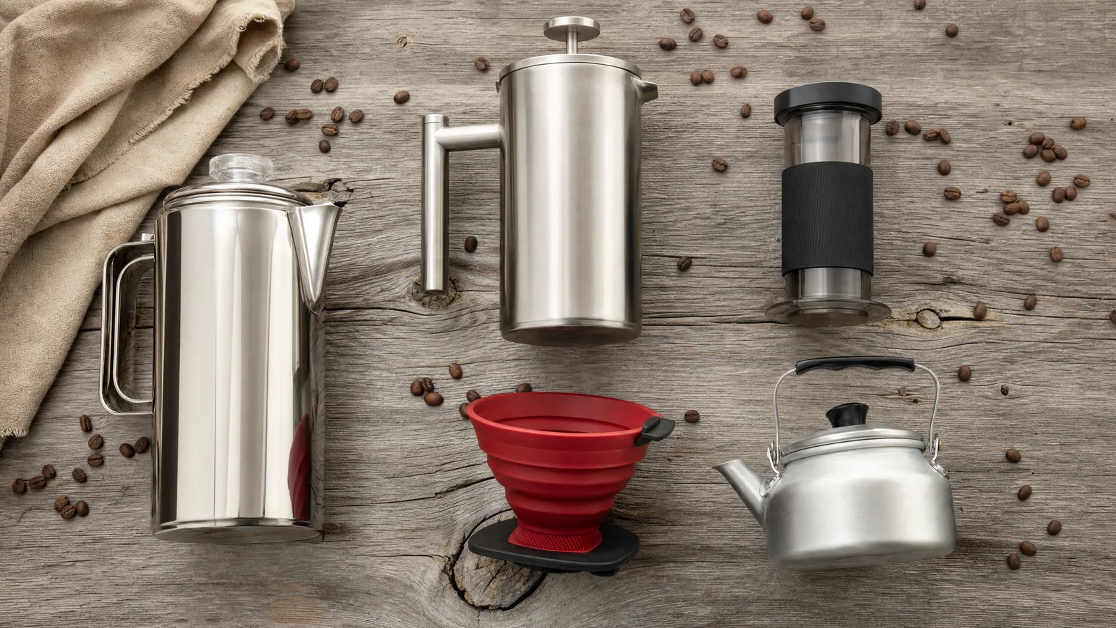 Overhead flat lay of camping coffee brewers including a percolator, insulated French press and collapsible pour-over dripper